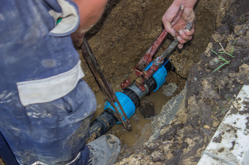 utility workers holds wrench and in trench repair the broken pipe for irrigation system